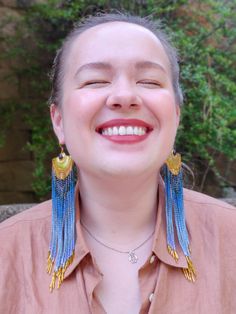 a woman smiling with her eyes closed and earrings hanging from her neck, wearing a pink shirt