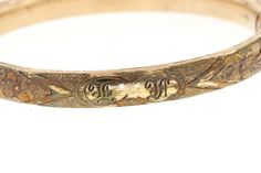 "This vintage hinged yellow gold filled bangle features a beautiful hand engraved floral and geometric design over the front half. The front has a monogram of what looks to be \"E M\". The back is plain. The bangle has been very well loved with some significant wear to the gold fill. The color is a rich buttery yellow gold. There is a push button hinged clasp that snaps closed tightly. The inner circumference is 7 inches and 8.25mm wide. The inside diameter is 2.4 inches. If the initials E and M Vintage Etched Yellow Gold Bangle, Vintage Adjustable Engraved Ceremonial Ring, Antique Engraved Yellow Gold Cuff Bracelet, Gold Etched Cuff Bracelet For Wedding, Victorian Gold Engraved Etched Ring, Victorian Gold Etched Engraved Ring, Victorian Etched Gold Engraved Ring, Heirloom Etched Bangle For Ceremonial Occasion, Ceremonial Heirloom Etched Bangle