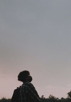 a man standing in the grass looking up at a kite