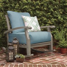 a wooden rocking chair sitting on top of a brick floor next to a green hedge