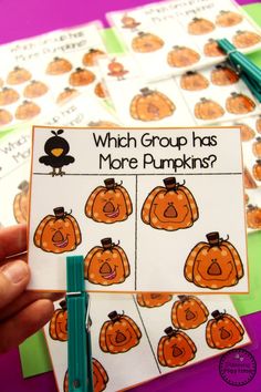 a hand holding up a card with pictures of pumpkins and words that read which group has more pumpkins?