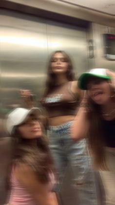 three girls are standing in front of a mirror and one girl is holding her hair