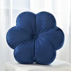 a blue flower shaped pillow sitting on top of a white chair in front of a window