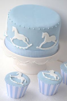 there is a blue cake with white horses on it and three cupcakes next to it