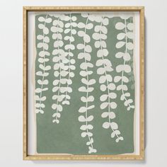 a green and white painting with leaves on the bottom framed in a wooden frame against a wall