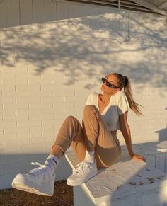 a woman sitting on top of a cement block next to a white wall and tree