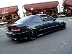 a black car is parked in front of some train cars