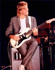 a man sitting on top of a stage with a guitar in his hand and another person standing behind him