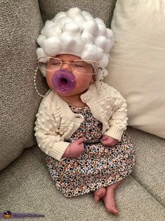 a baby doll with white hair and glasses sitting on a couch wearing a bubblegum wig