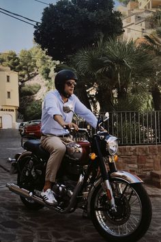 a man riding on the back of a motorcycle down a cobblestone street next to palm trees