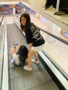 two girls on an escalator looking at their cell phones while one girl sits on the ground