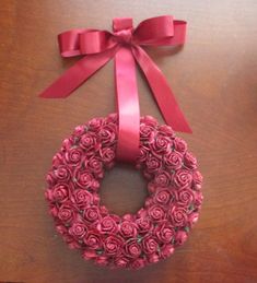 a pink rose wreath on a table with a red ribbon hanging from it's center