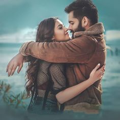 a man and woman embracing each other with the ocean in the back ground behind them