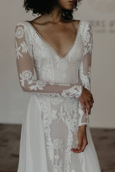 a woman wearing a white wedding dress with long sleeves and sheer lace on the shoulders