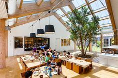 children are sitting at tables in the middle of a room with large windows and wooden beams