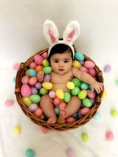 a baby in a basket with easter eggs and bunny ears on it's head