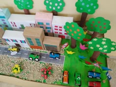 a toy town with cars, trucks and trees on the ground next to a building