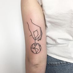 a woman's arm with a black and white outline of a hand holding the earth