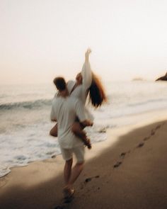 a man carrying a woman on his back while walking along the beach