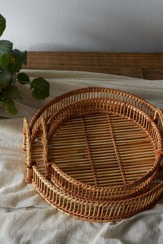 two wicker trays sitting on top of a bed next to a potted plant