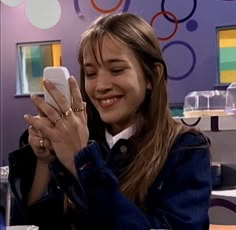 a woman holding a cell phone in her right hand while sitting at a table with other people