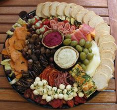 a platter filled with meats, cheeses and crackers on top of a wooden table