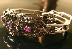 "Just gorgeous vintage estate antiqued sterling silver, marcasite and amethyst hinged bracelet, featuring three heavily faceted and prong set round soft purple colored amethysts surrounded by floral shapes encrusted with dazzling marcasite; and a contrasting highly polished open silver work design at sides and back. Hinged bracelet has wearable (interior) length of approximately 6 1/2\" and width of 13/16\"; substantial piece with total weight of 30.7 g. Box clasp closure with safety clasp on to Antique Silver Jeweled Jewelry, Antique Jeweled Silver Jewelry, Vintage Silver Bracelet With Diamond Accents, Victorian Silver Bracelets With Jewels, Antique Silver Gemstone Bracelet, Art Deco Amethyst Silver Jewelry, Art Deco Silver Amethyst Jewelry, Silver Amethyst Art Deco Jewelry, Formal Marcasite Gemstone Jewelry