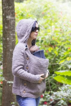 a woman is walking through the woods with her cat on her shoulder and wearing a hoodie