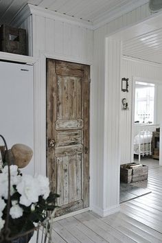 an open door in a white room next to a vase with flowers