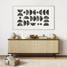 an abstract painting hangs on the wall next to a wooden cabinet with vases and bowls