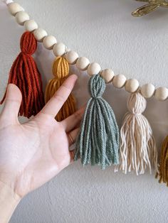 a person is holding their hand out in front of some tassels on a string