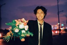 a young man in a suit and tie standing next to a bouquet of flowers at night