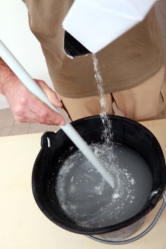 a man is pouring water into a black pot with white handles and an ointment in it