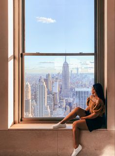 a woman sitting on a window sill looking out at the cityscape and skyscrapers