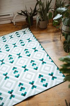 a green and white quilt sitting on top of a wooden floor next to potted plants