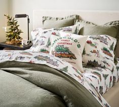 a bed with christmas themed pillows on it and a small tree in the corner next to it