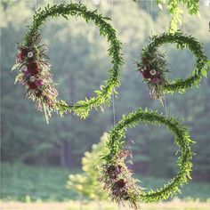 three circular wreaths hanging from the ceiling in front of some trees and grass with flowers on them