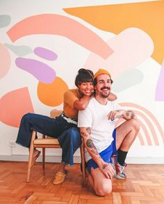 a man and woman sitting on a chair in front of a colorful wall