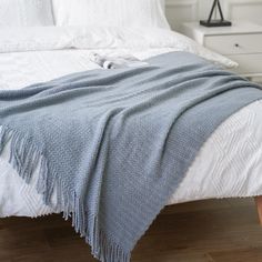 a white bed with a blue blanket on top of it next to a night stand