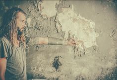 a man with dreadlocks holding out his hand in front of a dirty wall