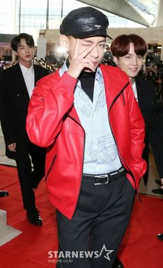 a man in a red leather jacket and hat walking down a red carpeted area