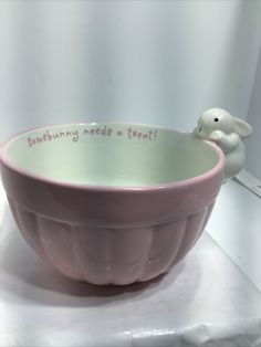 a pink bowl with writing on it and a small white bird figurine next to it