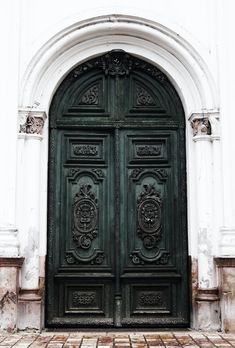 an ornately decorated green door in front of a white building with brick flooring