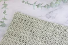 the crocheted blanket is next to some green leaves on a marble countertop