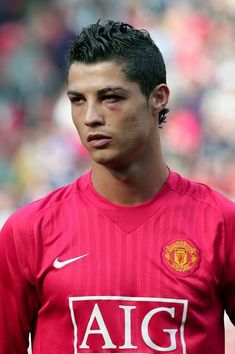 a young man in a red shirt standing on a soccer field with his head turned to the side