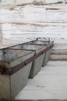 three metal containers sitting on top of a white table next to a wooden plank wall