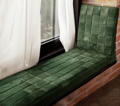 a green bench sitting in front of a brick wall next to a window with white curtains