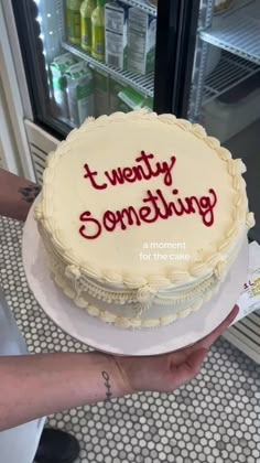 a cake with the words twenty something on it is being held by a woman in front of an open refrigerator