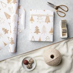 wrapping paper, twine and other crafting supplies on a white table with gold foil trees