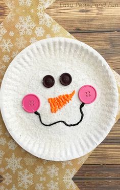 a paper plate with a snowman made out of buttons and carrots on it